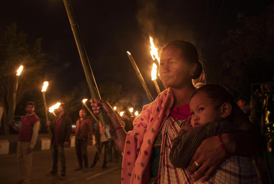 An Indian tribal woman carries a child as she participates in a torch light procession to protest against the Citizenship Amendment Bill (CAB) in Gauhati, India, Monday, Dec. 9, 2019. The bill that seeks to grant Indian citizenship to non-Muslim refugees from Pakistan, Bangladesh and Afghanistan is being debated in the Indian Parliament. (AP Photo/Anupam Nath)