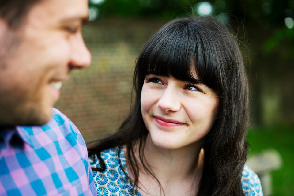 Woman looking at man, both smiling, outside