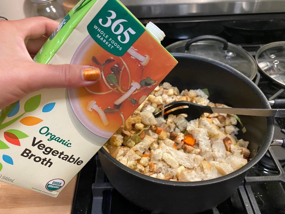 hand pouring veggie broth into an air fryer container with stuffing ingredients