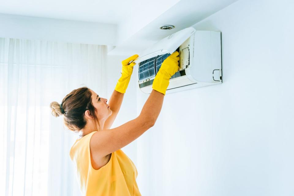 Woman wearing yellow rubber gloves changing the filter in a split-system air conditioner