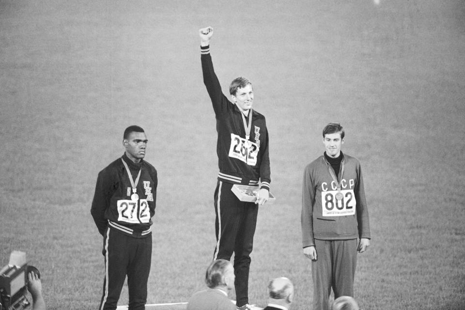 FILE - Gold medal winner Dick Fosbury raises his arm on the victor's podium of the Olympic stadium, Oct. 20, 1968, in Mexico City. At left is silver medalist Ed Caruthers of the U.S. and at right is bronze medalistr Valentin Gavrilov of Russia. Fosbury, the lanky leaper who completely revamped the technical discipline of high jump and won an Olympic gold medal with his “Fosbury Flop,” has died after a recurrence with lymphoma. Fosbury died Sunday, March 12, 2023, according to his publicist, Ray Schulte. He was 76. (AP Photo/File)