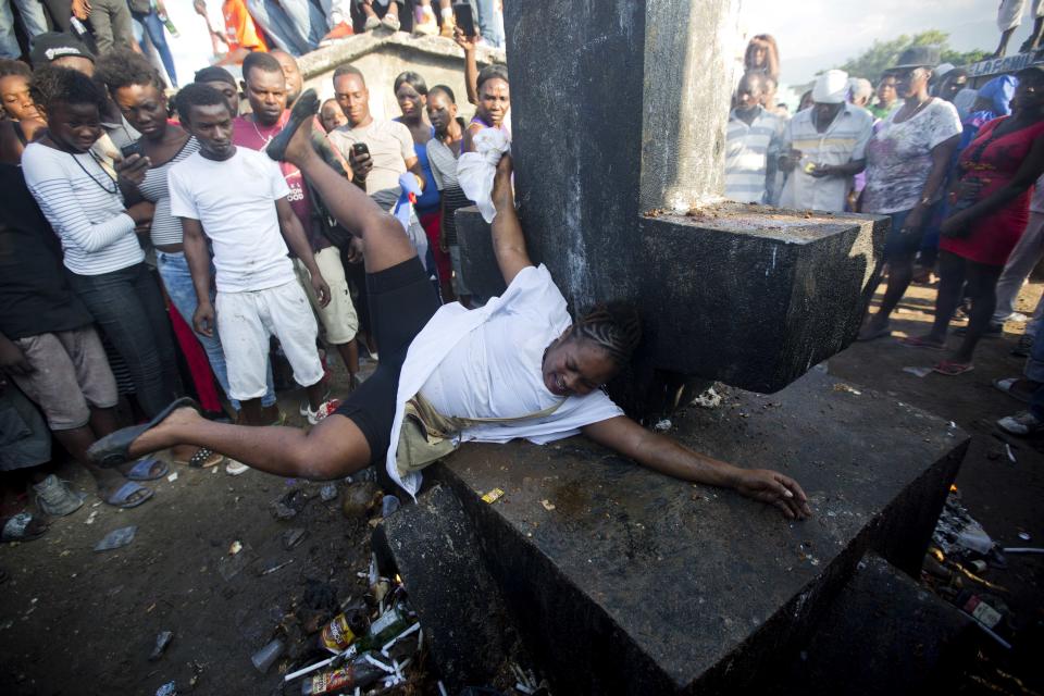 In this Nov. 1, 2018 photo, a voodoo believer who is supposed to be possessed with Gede spirit perform rituals on Baron Samedi's tomb during the annual Voodoo festival Fete Gede at Cite Soleil Cemetery in Port-au-Prince, Haiti. Baron Samedi is also considered by Haitian voodooists as the wisest adviser, protector of children and the last hope for the sick. ( AP Photo/Dieu Nalio Chery)