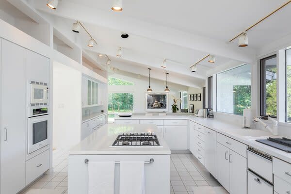 The all-white kitchen is fitted with long countertops, ample cabinetry, and a central island.