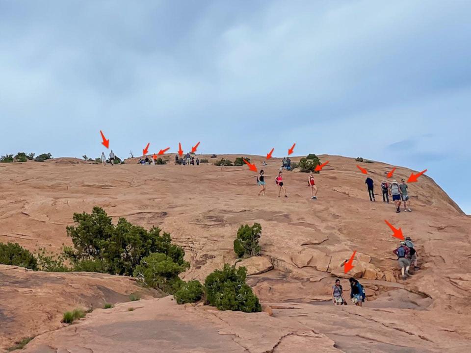 Arrows point to crowds of people hiking the trail to Arches' delicate arch.