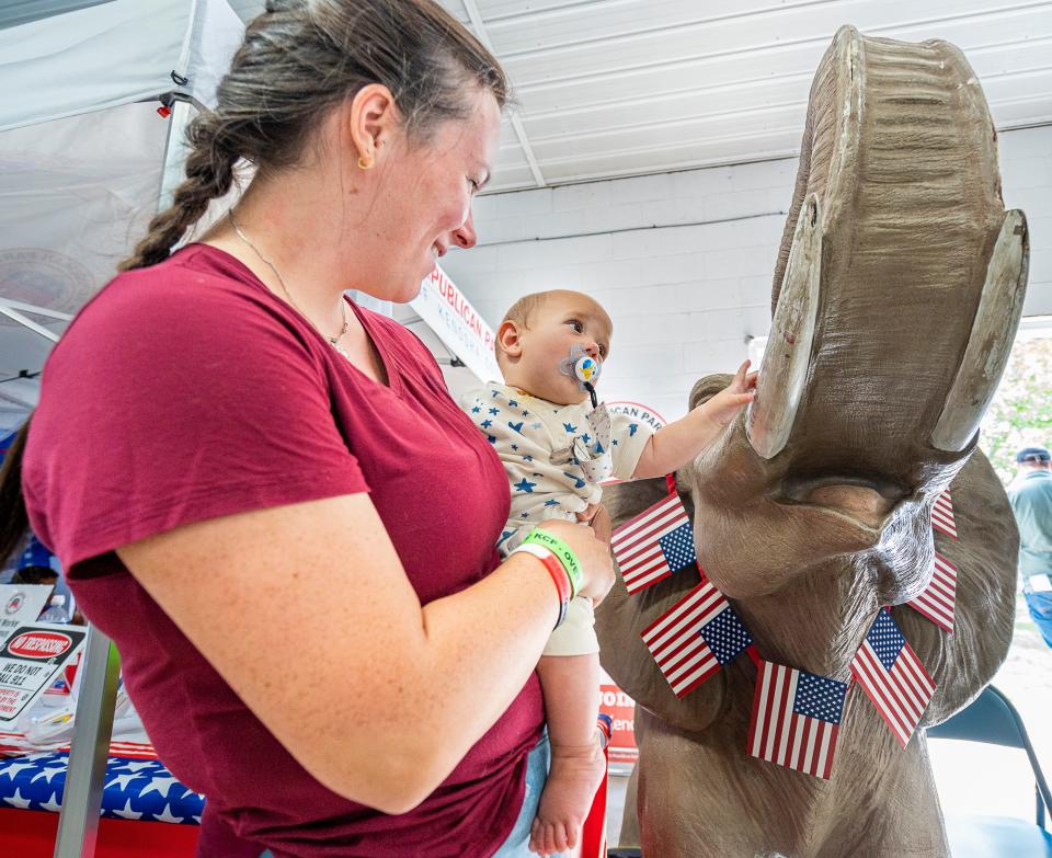 Julie Bennett of Salem carries her 6-month old Augustine Bennett who reaches out to "Dutch" the elephant at the Republican Party of Kenosha County booth on Friday August 18, 2023 at the Kenosha County Fairgrounds in Wilmot, Wis.