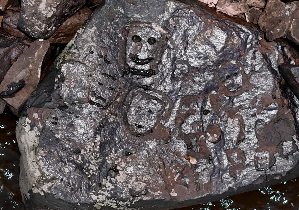 An engraving in a rock placed on a muddy river bank looks like a smiling face