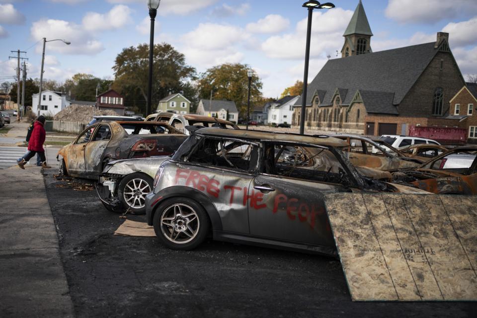 People walk past burnt vehicles in Kenosha, Wis., Friday, Oct. 30, 2020. The trouble in Kenosha began on Aug. 23 when a Kenosha police officer, responding to a call about a domestic dispute, was caught on video shooting Jacob Blake repeatedly in the back at close range. Blake, a Black man, survived but is partially paralyzed. The August shootings have spurred a spike in political involvement in Kenosha, with the formation of activism and waves of new voters signing up. (AP Photo/Wong Maye-E)