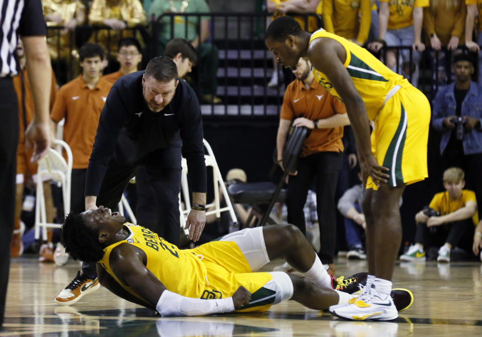 FILE - Baylor forward Jonathan Tchamwa Tchatchoua, bottom, is checked on Texas head coach Chris Beard, top left, and Baylor guard Dale Bonner, right after falling to the court with an apparent leg injury during the first half of an NCAA college basketball game on Saturday, Feb. 12, 2022, in Waco, Texas. Tchamwa Tchatchoua sees himself as a “walking miracle” after getting back on the court for 14th-ranked Baylor nearly a full year after a gruesome knee injury that many people thought would end his career. (AP Photo/Ray Carlin)