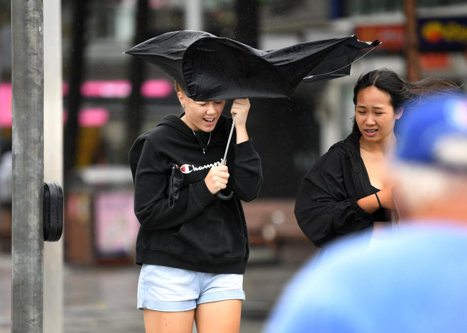 A teenage girl struggles with her umbrella in stormy conditions at Surfers Paradise on the Gold Coast.