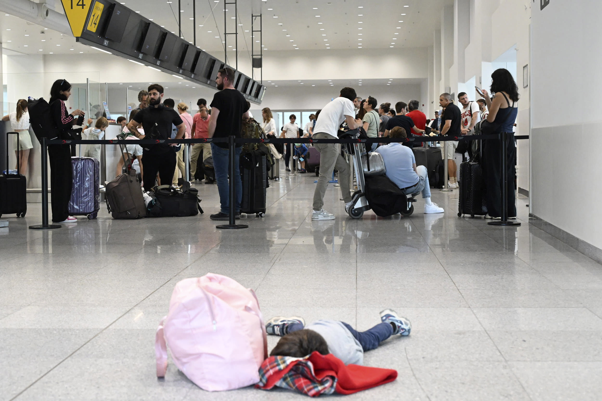 A little boy lies on the ground as travelers queue at Brussels airport.