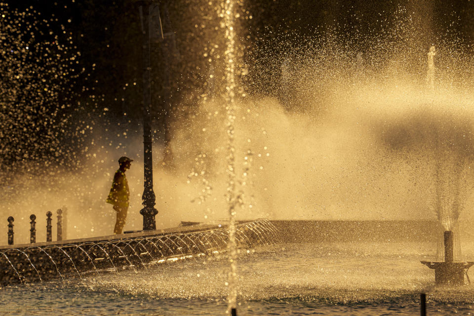 A municipal worker cools off standing next to a city fountain in Bucharest, Romania, Thursday, July 11, 2024, as temperatures exceeded 39 degrees Celsius (102.2 Fahrenheit). The national weather forecaster issued a red warning for the coming week, as temperatures are expected to exceed 40 degrees Celsius (104 Fahrenheit). (AP Photo/Vadim Ghirda)