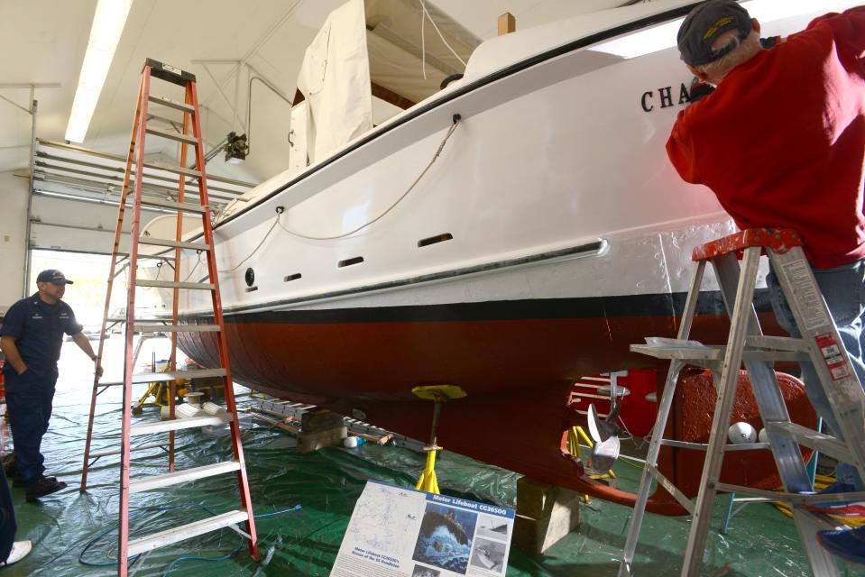 Coast Guard Station Chatham Senior Chief Ross Comstock, left, checks in on Wednesday on the progress of the famous rescue boat CG36500 getting a facelift in a storage barn before its launch into Rock Harbor on Tuesday. Volunteer Howard Gostin letters the stern of the boat, at right.