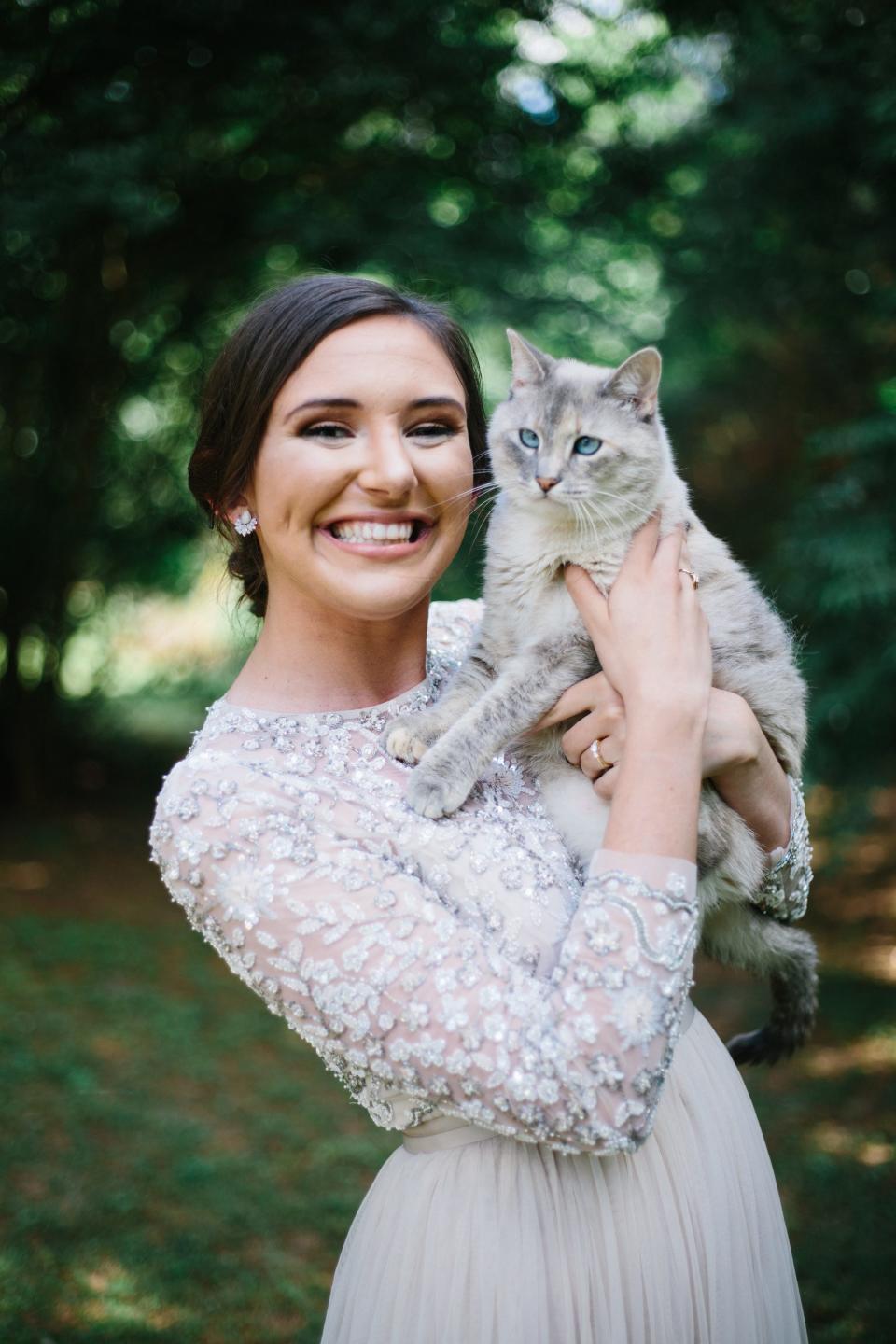 A bride poses with a cat in a wooded area.