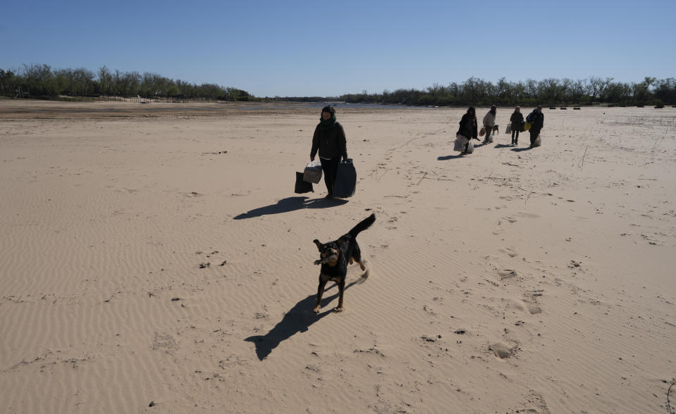 FILE - People who live in the fishing village of Espinillo Island walk their goods across the Old Parana River delta now that boats can't reach their community and others, amid a drought that turned the river into a sand bank, across the river from Rosario, Argentina, July 29, 2021. Climate change isn’t causing the multi-year drought that is devastating parts of Argentina, Uruguay, Brazil and Bolivia, but warming is worsening some of the dry spell’s impacts, a new study says. (AP Photo/Victor Caivano, File)