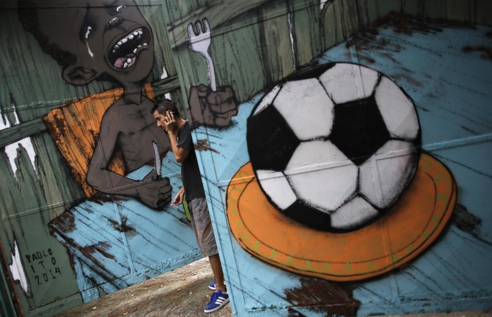 Brazilian artist Paulo Ito talks on his mobile phone next to graffiti he painted referencing the 2014 World Cup, on the door of a public schoolhouse in Sao Paulo May 22, 2014. The city of Sao Paulo will host the opening match of the 2014 Brazil World Cup. REUTERS/Nacho Doce (BRAZIL - Tags: SPORT SOCCER WORLD CUP SOCIETY TPX IMAGES OF THE DAY)