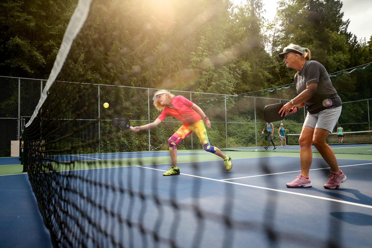 Susan Crossland, of Bremerton, hits the ball over the net while pickleball doubles partner Shelley Agostino, of Seabeck, looks on as the two play a game against DeDe Grutz and Laura Miller at the Seabeck Community Center courts on Wednesday.