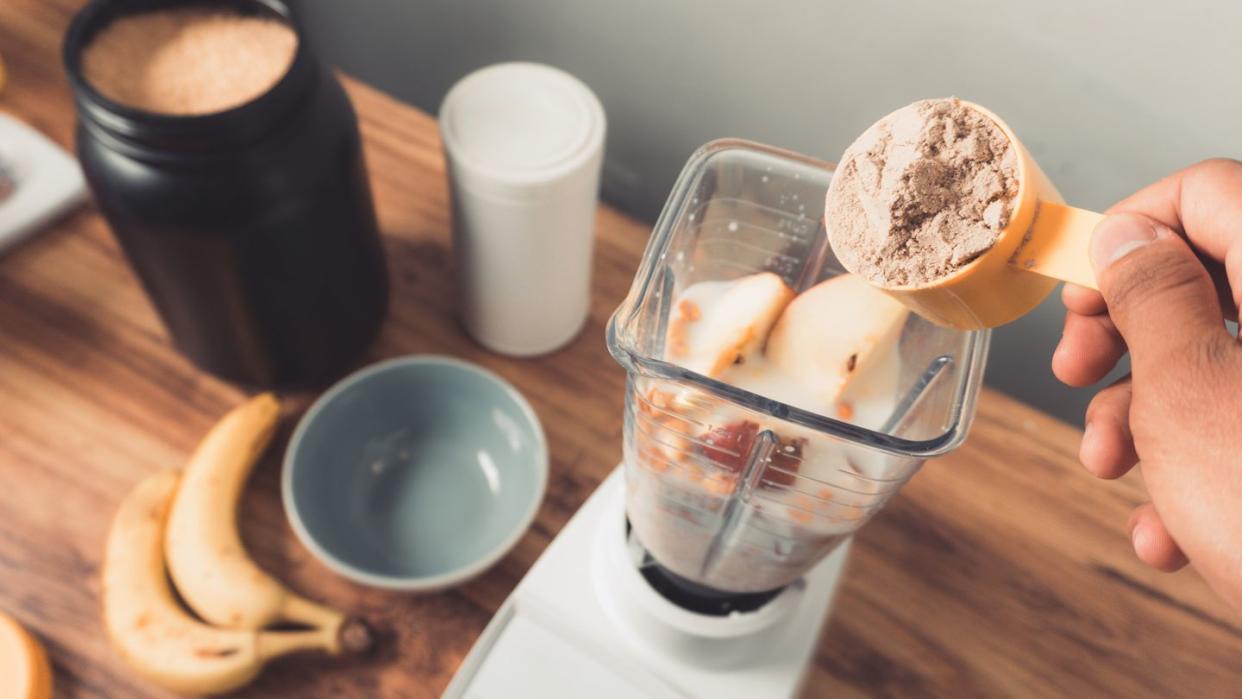 hand holding a protein scoop over blender with smoothie