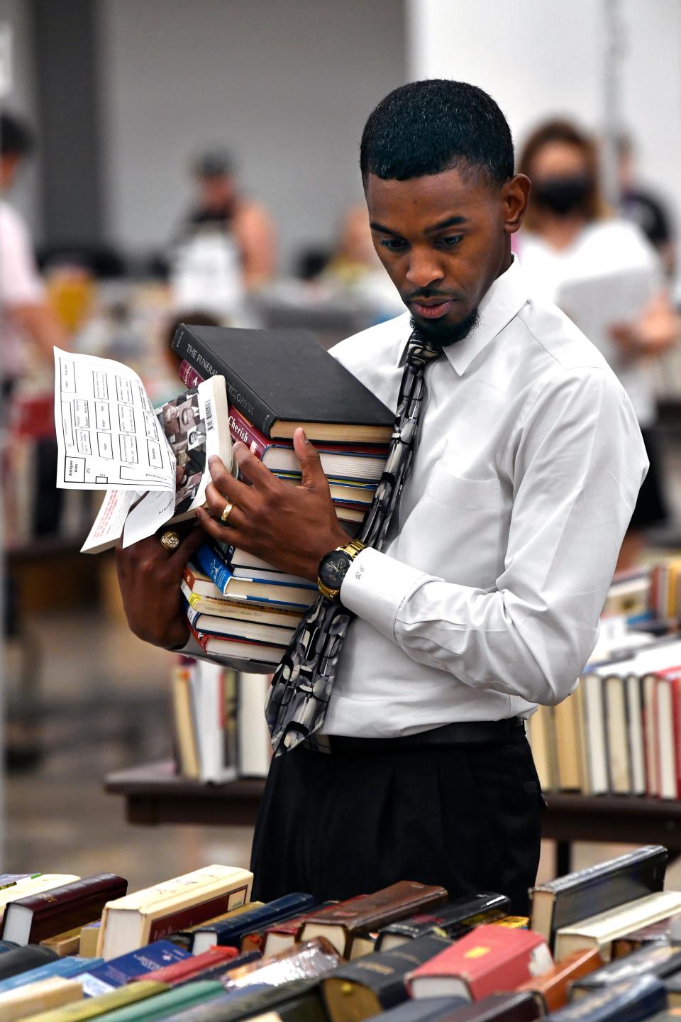 Justin Garland cradles a stack of books as he peruses other titles for him to add to it during Friday's book sale.