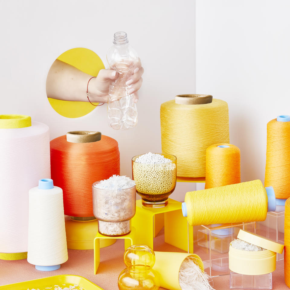 A hand holds a plastic bottle to show how the waste is transformed into Repreve fibers, shot in a punchy orange and yellow photo arrangement of fibers and threads.  