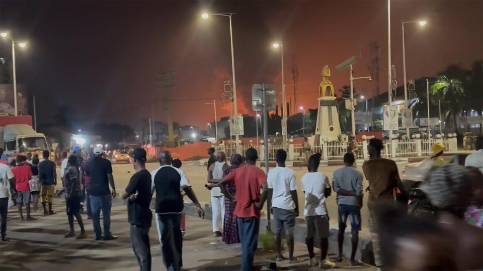 In this image made from video, residents watch a plume of smoke from a burning oil depot, in Conakry, Guinea, Monday, Dec. 18, 2023. An explosion and inferno at Guinea’s main fuel depot in the capital of Conakry has left several people dead or injured. Guinea’s presidency says the fire broke out at the Guinean Petroleum Company depot shortly after a massive explosion past midnight Sunday. (AP Photo)