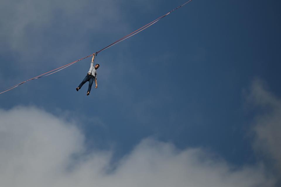 Highliner Nathan Paulin hangs on a slackline as he crosses a distance of 500 metres between Morro da Babilônia and Morro da Urca at Praia Vermelha, beside Sugarloaf Mountain, in Rio de Janeiro, Brazil on December 4, 2021. - The performance is part of the Les Traceurs project conceived by French choreographer Rachid Ouramdane, current director of the Theater Chaillot, from Paris. (Photo by ANDRE BORGES / AFP) (Photo by ANDRE BORGES/AFP via Getty Images)