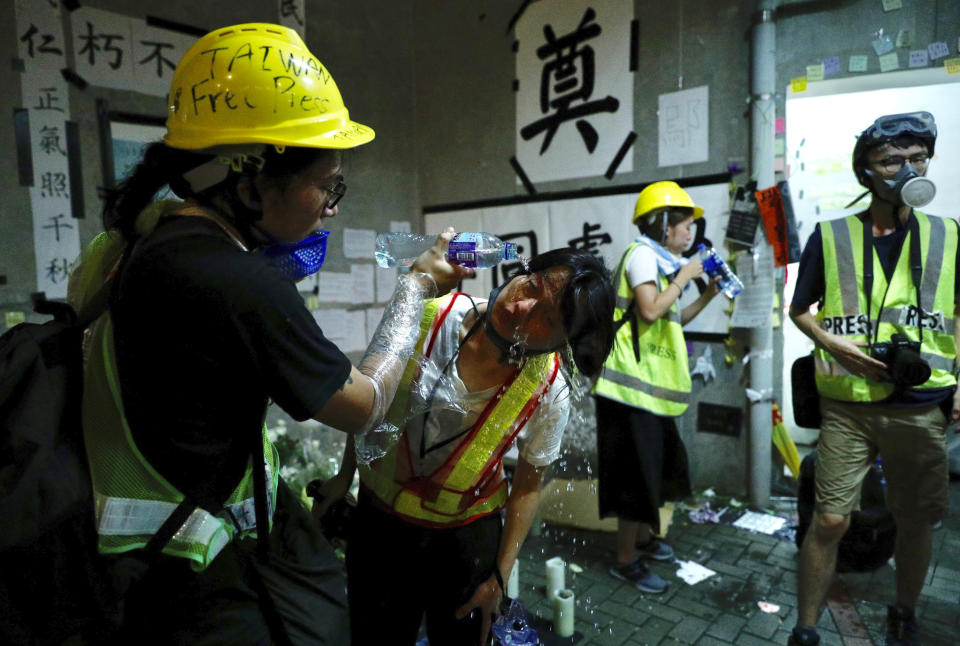 File - In this July 2, 2019, file photo, protester pours water into the eyes of a fellow protester after police release tear gas to clear them from the Legislative Council in Hong Kong, during the early hours. Protesters in Hong Kong took over the legislature's main building Friday night, tearing down portraits of legislative leaders and spray painting pro-democracy slogans on the walls of the main chamber. (AP Photo/Vincent Yu, File)