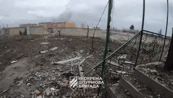 A moving image showing a man firing a rifle in a ruined cityscape.