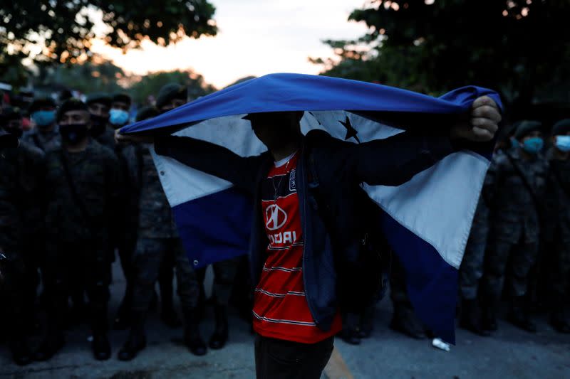 A Honduran migrant trying to reach the U.S. holds a Honduran flag while standing in front of Guatemalan soldiers blocking a road to stop migrants from reach the Mexico's border, in San Pedro Cadenas