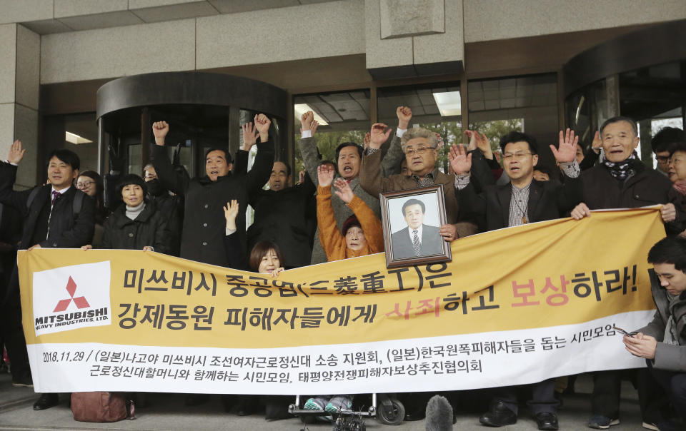 FILE - In this Nov. 29, 2018, file photo, South Korean victims of Japan's forced labor and their family members raise their hands in celebration after the Supreme Court's ruling ordering Japan's Mitsubishi Heavy Industries to compensate them in Seoul, South Korea. Seoul has accused Tokyo of weaponizing trade to retaliate against South Korean court rulings calling for Japanese companies to offer reparations to South Koreans forced into slave labor during World War II. The signs read: "Mitsubishi Heavy Industries apologizes and compensates to victims."(AP Photo/Ahn Young-joon, File)