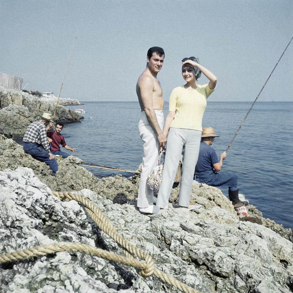 FILE - In this 1965 file photo American actor Tony Curtis poses holding hands with his wife Christine Kaufmann on the rocky beach of Cannes, France. Christine Kaufmann died Tuesday, March 28, 2017. She was 72. (AP Photo)