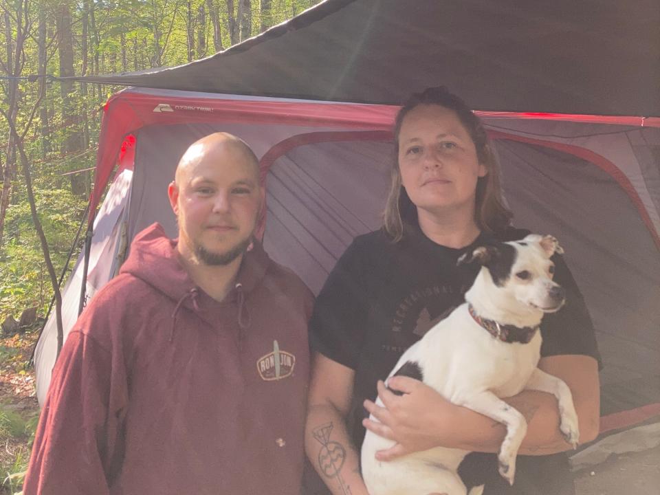 Lauren and Benji Bahre stand in front of their tent with Lauren carrying the couple's dog, Ellie, in her arms.