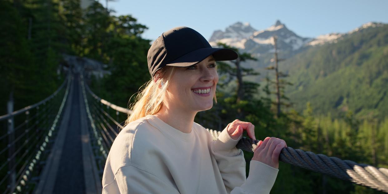  Mel Monroe smiling and looking out to the distance as she stands on a bridge. 