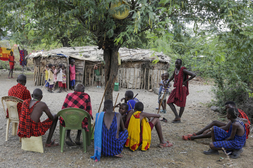 In this photo taken on Thursday, April 9, 2020, Maasai gather under a tree in their village in Kajiado County in Kenya. The Maasai, a semi-nomadic indigenous group in Kenya and Tanzania, have been forced to halt important rituals that bring clans together due to the coronavirus, including the graduation of warriors into young men who can marry and own property. (AP Photo/Khalil Senosi)