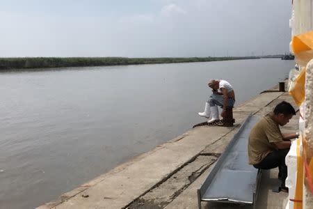 People sit at Yicuomao port in Dandong, Liaoning province, China, August 8, 2017. The shore of North Korea is seen across the water. REUTERS/Philip Wen