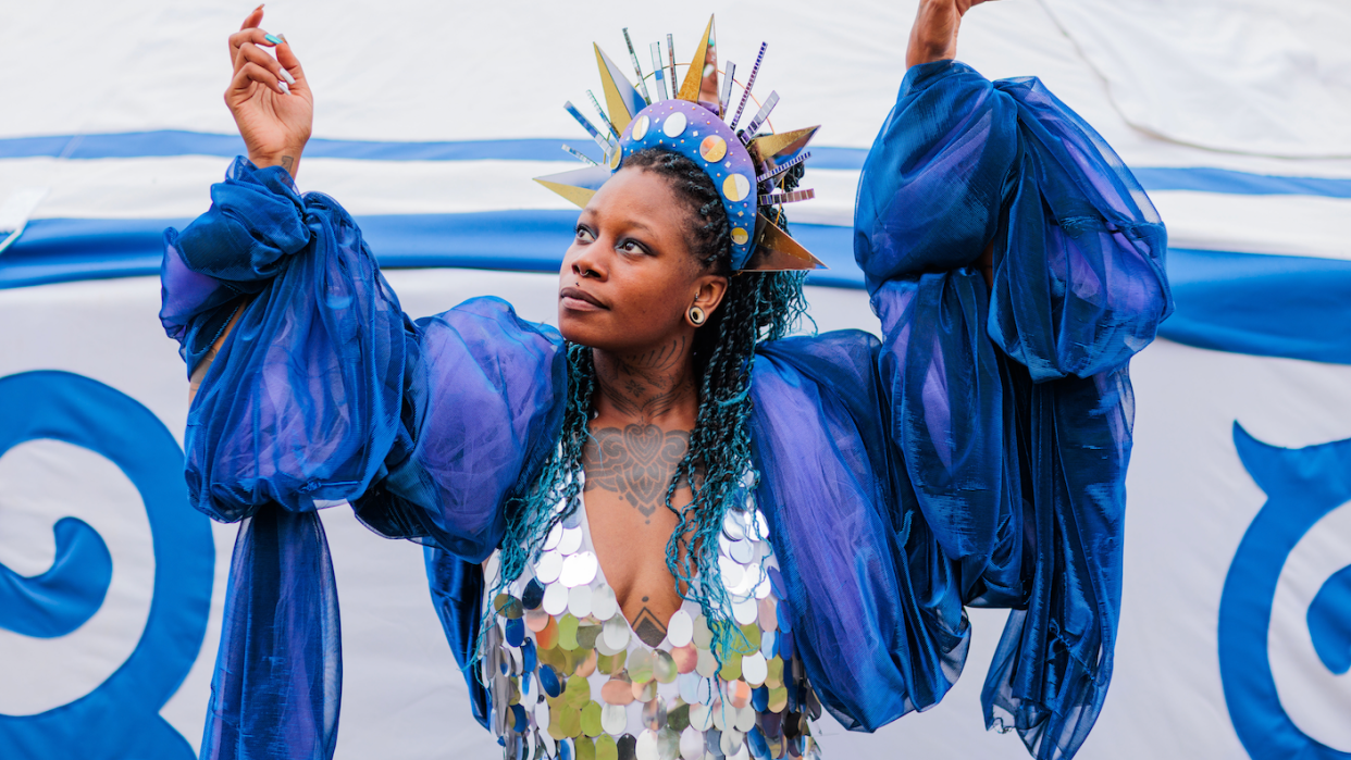 A woman wearing a sequn top draped in blue fabric and a colourful crown