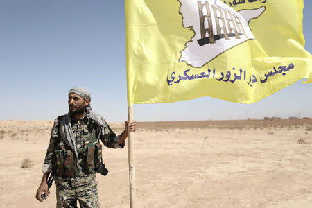 A fighter from Deir al-Zor military council which fights under the Syrian Democratic Forces (SDF) holds the council's flag in the village of Abu Fas, Hasaka province, Syria September 9, 2017. REUTERS/Rodi Said