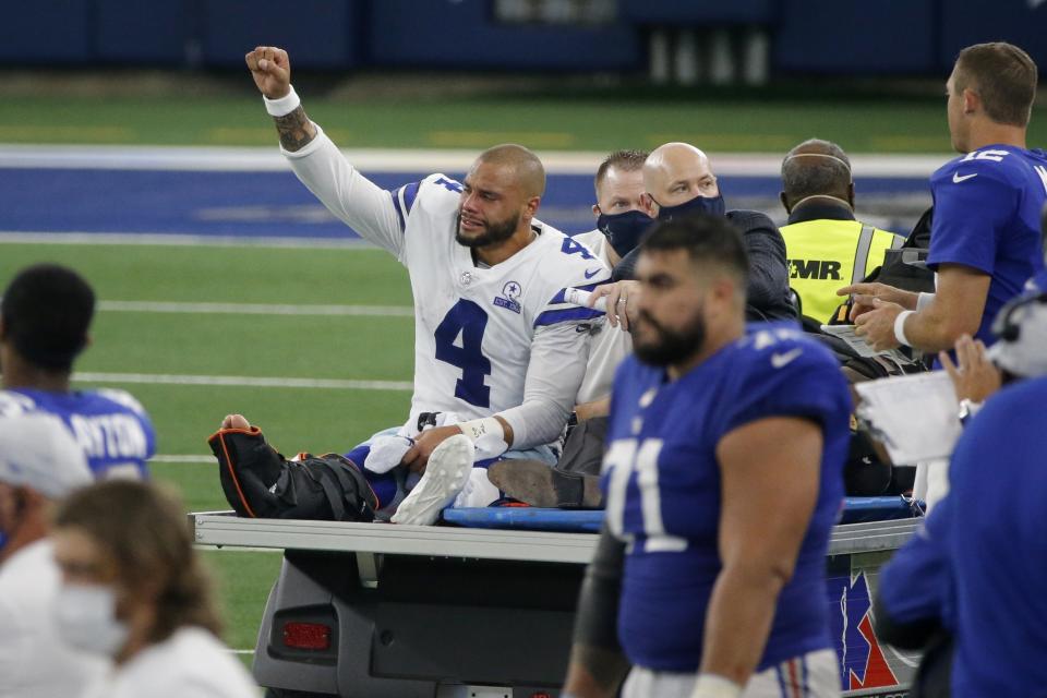 FILE - In this Oct. 11 , 2020, file photo, Dallas Cowboys quarterback Dak Prescott (4) lifts his fist to cheers from fans as he is carted off the field after suffering an injury during the second half of the team's NFL football game against the New York Giants in Arlington, Texas. Prescott was off to a fast start, becoming the first player in NFL history to pass for at least 450 yards in three straight games. But he suffered a compound fracture and dislocated right ankle against the Giants and missed the rest of the season. (AP Photo/Michael Ainsworth, File)