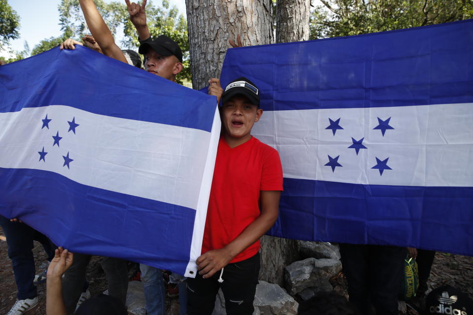 Honduran migrants trying to reach the United States hold up Honduran flags while they are stopped by Guatemalan National Police after crossing the Honduran border, in Morales, Guatemala, Wednesday, Jan. 15, 2020. Migrants in the group said they left Honduras very late Tuesday, around midnight. (AP Photo/Moises Castillo)