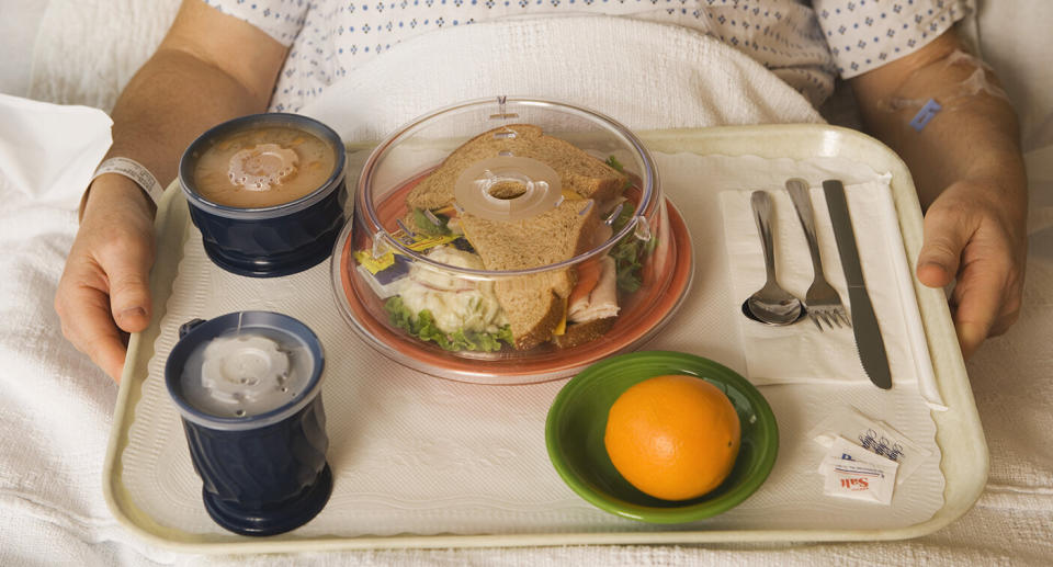 A hospital patient holing a tray of food, including a sandwich.