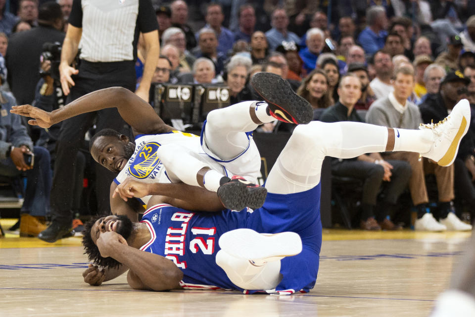 Golden State Warriors forward Draymond Green (23) falls over Philadelphia 76ers center Joel Embiid (21) on an offensive foul by Embiid during the first half of an NBA basketball game, Tuesday, Jan. 30, 2024, in San Francisco. (AP Photo/D. Ross Cameron)