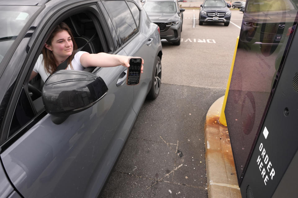 Alexis Bogan, whose speech was impaired by a brain tumor, uses mobile phone with an app that features a voice-cloning tool to order a drink at a Starbucks drive-thru Monday, April 29, 2024, in Lincoln, R.I. Doctors treating Bogan are recreating her original voice using a voice-cloning tool from OpenAI. (AP Photo/Steven Senne)