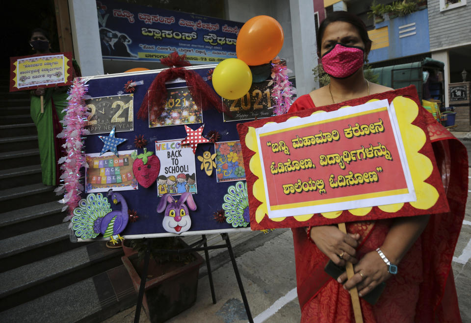 A teacher wearing face mask as a precaution against the coronavirus holds a placard that reads 'let's chase away coronavirus pandemic and get back students to school for education' outside Blossoms High School in Bengaluru, India, Friday, Jan. 1, 2021. The southern state of Karnataka on Friday opened schools for students of grade 10 and 12 after a gap of more than nine months. India has more than 10 million cases of coronavirus, second behind the United States. (AP Photo/Aijaz Rahi)