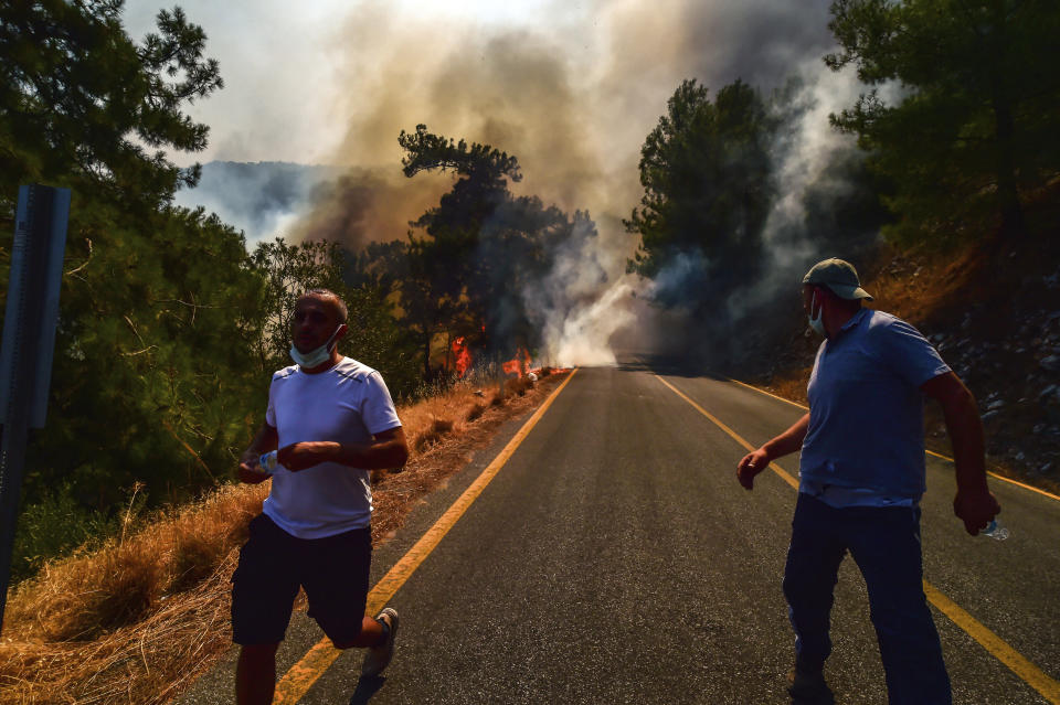 People run away as the wildfires engulf an area near the seashore, forcing people to be evacuated by boats, in Bodrum, Mugla, Turkey, Sunday, Aug. 1, 2021. Wildfires in the Turkish holiday destinations of Antalya and Mugla are still raging as firefighters worked to battle the blazes for a fifth day. Authorities warned tourists and residents to keep evacuating Turunc, a town in the seaside resort of Marmaris, and navy ships waited in the sea there to see if a bigger evacuation was needed. (Ismail Coskun/IHA via AP)