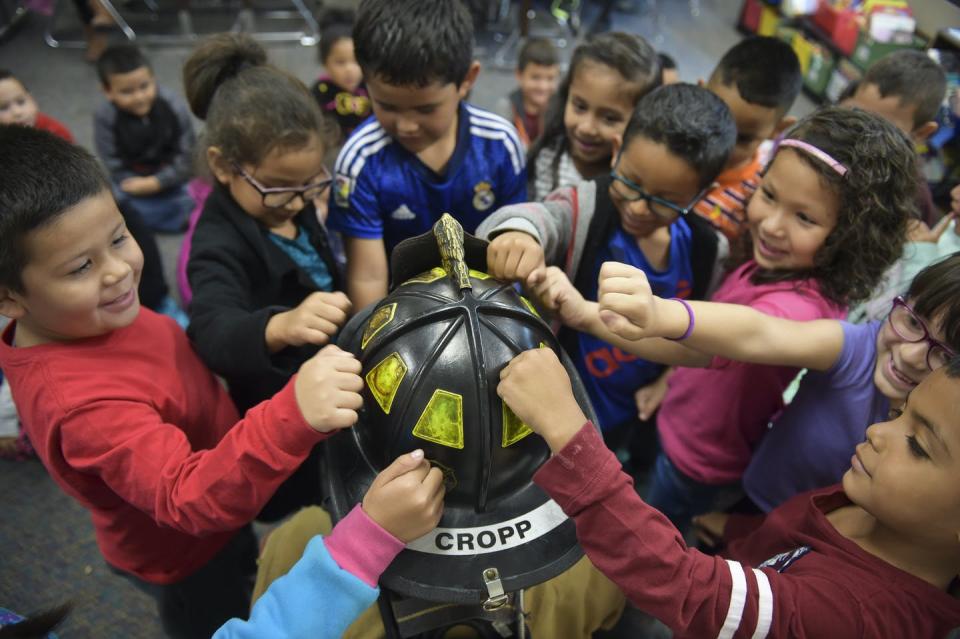 A group of children place their hands on a fireman's hat.