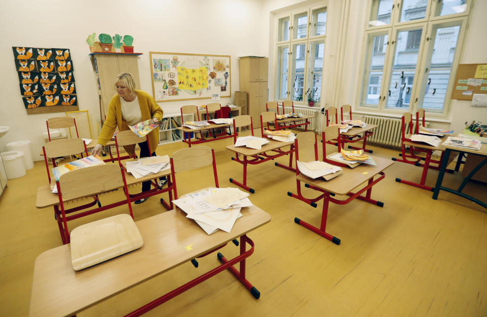 A teacher sorts drawings in an empty classroom at a closed school in Prague, Czech Republic, Wednesday, Oct. 14, 2020. Amid widespread efforts to curb the new wave of coronavirus infections in one of the hardest hit European countries, the Czech Republic closed again all its schools on Wednesday. (AP Photo/Petr David Josek)