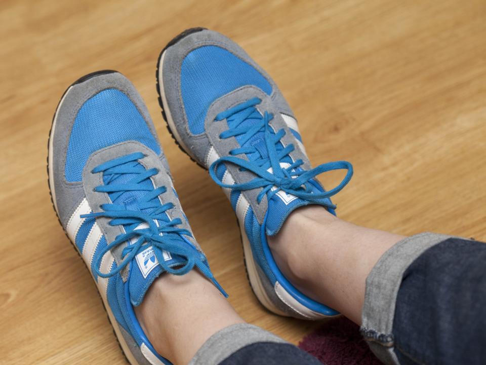 Woman wearing blue and grey and white Adidas suede sneakers.