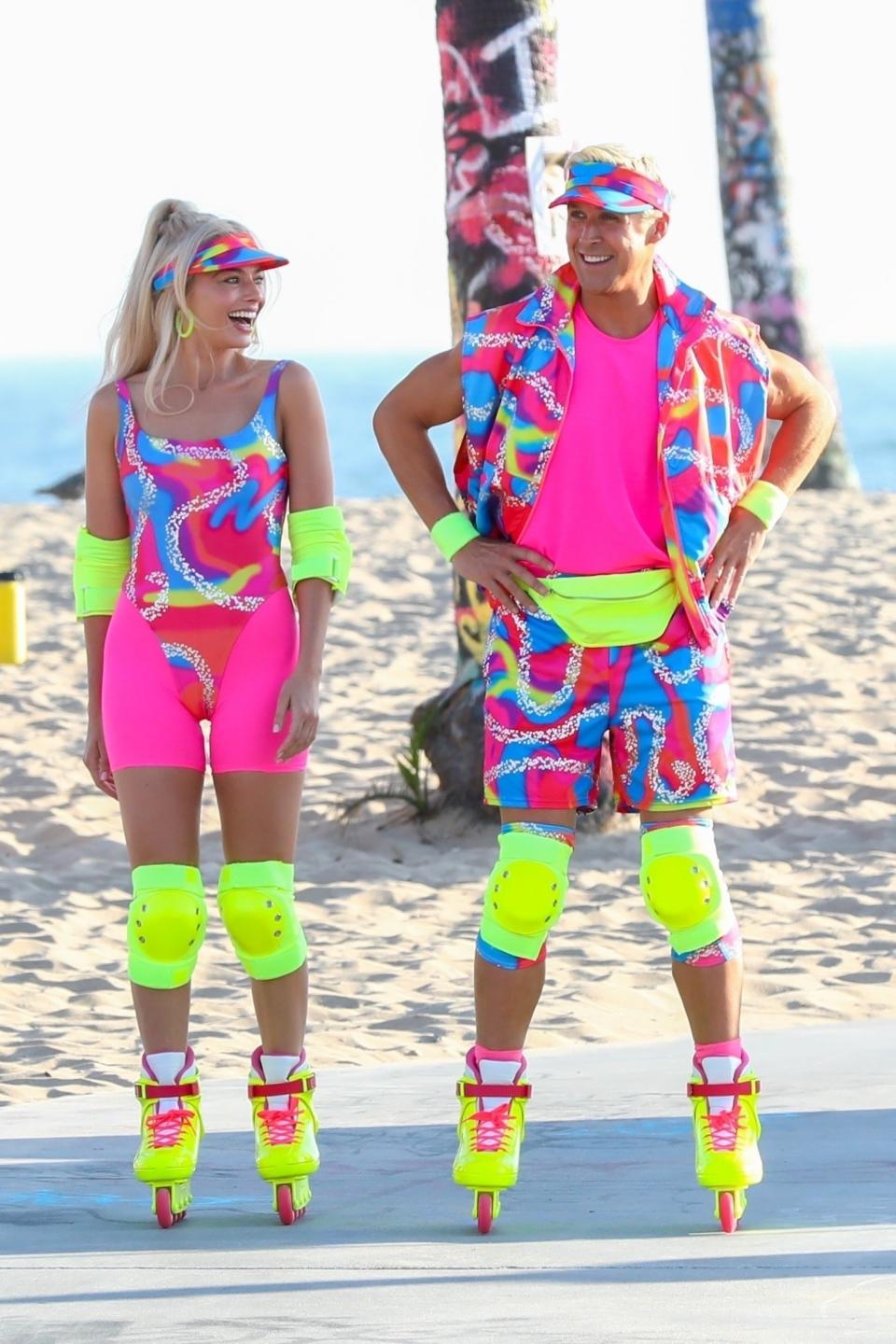 Margot still in rollerblades, now joined by Ryan; they're both wearing matching neon outfits with bright knee pads and rollerblades