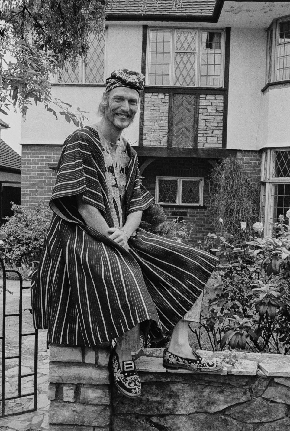 Drummer Ginger Baker wearing traditional African robes while sitting on a gate post, pictured during the promotion of the 'Sunday Omnibus' showing of his documentary 'Ginger Baker in Africa', June 1973. (Photo by Clive Barda/Radio Times via Getty Images)