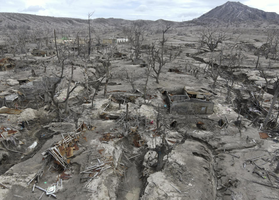 Shredded trees and the shells of homes lie half buried in mud near the Taal volcano almost a year after it erupted in Batangas province, a popular tourist destination just south of Manila, Philippines, on Jan. 10, 2021. (AP Photo/Aaron Favila)