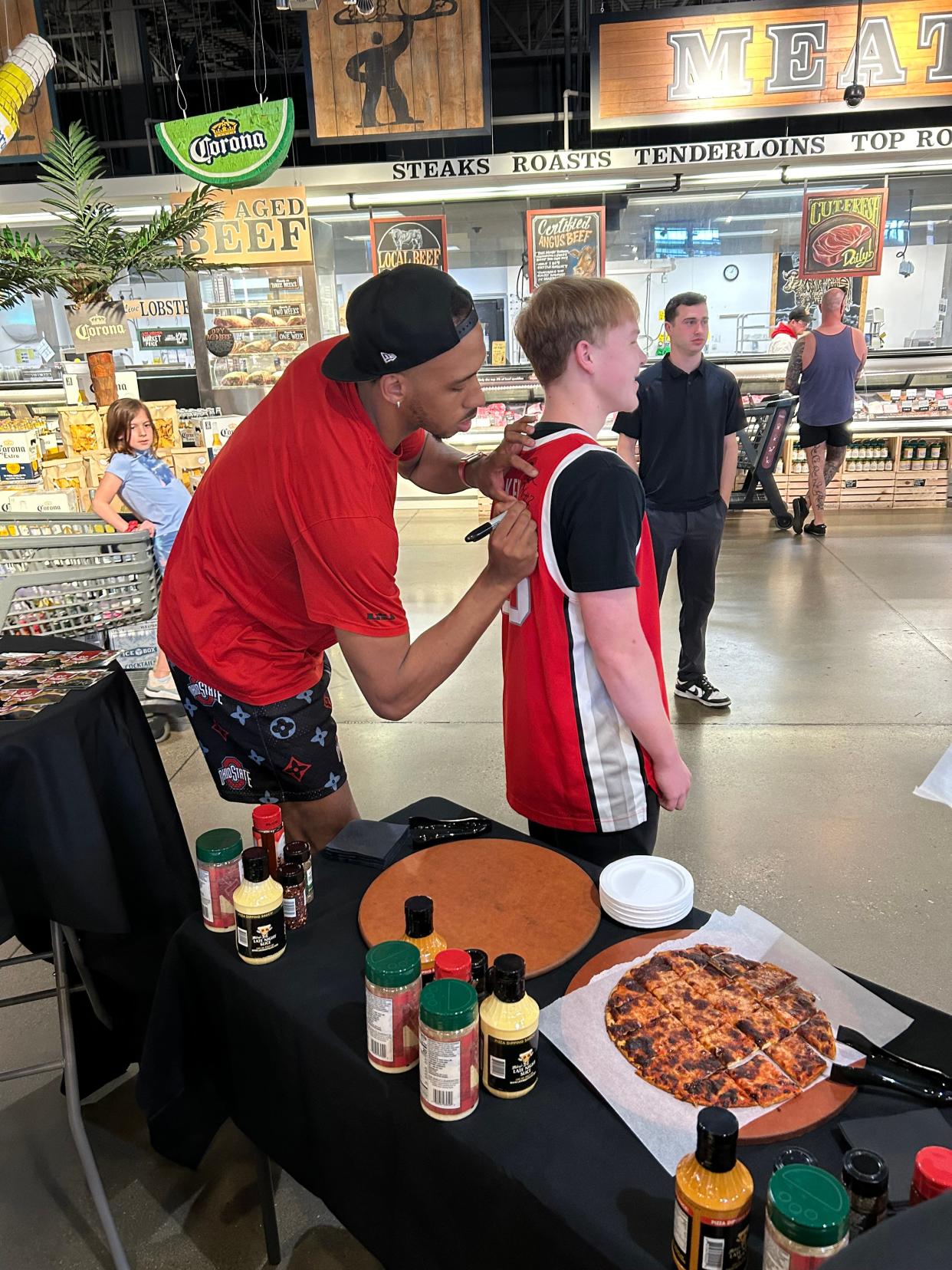 Former Ohio State center Zed Key signs a No. 23 jersey worn by Jack Landes, a fan who plays basketball at Whetstone, at a public meet-and-greet at Giant Eagle on W. 3rd Ave. on April 14, 2024.